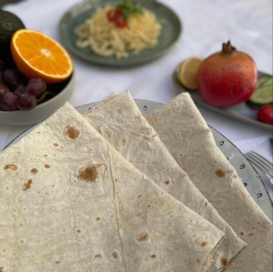 Gefaltete Blätter Köy Yufkası auf einer Glasschale, dahinter Obst auf einem gedeckten Tisch